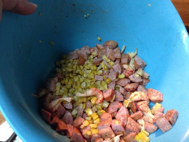 A bowl with corn, crawfish tail meat, and sausage.